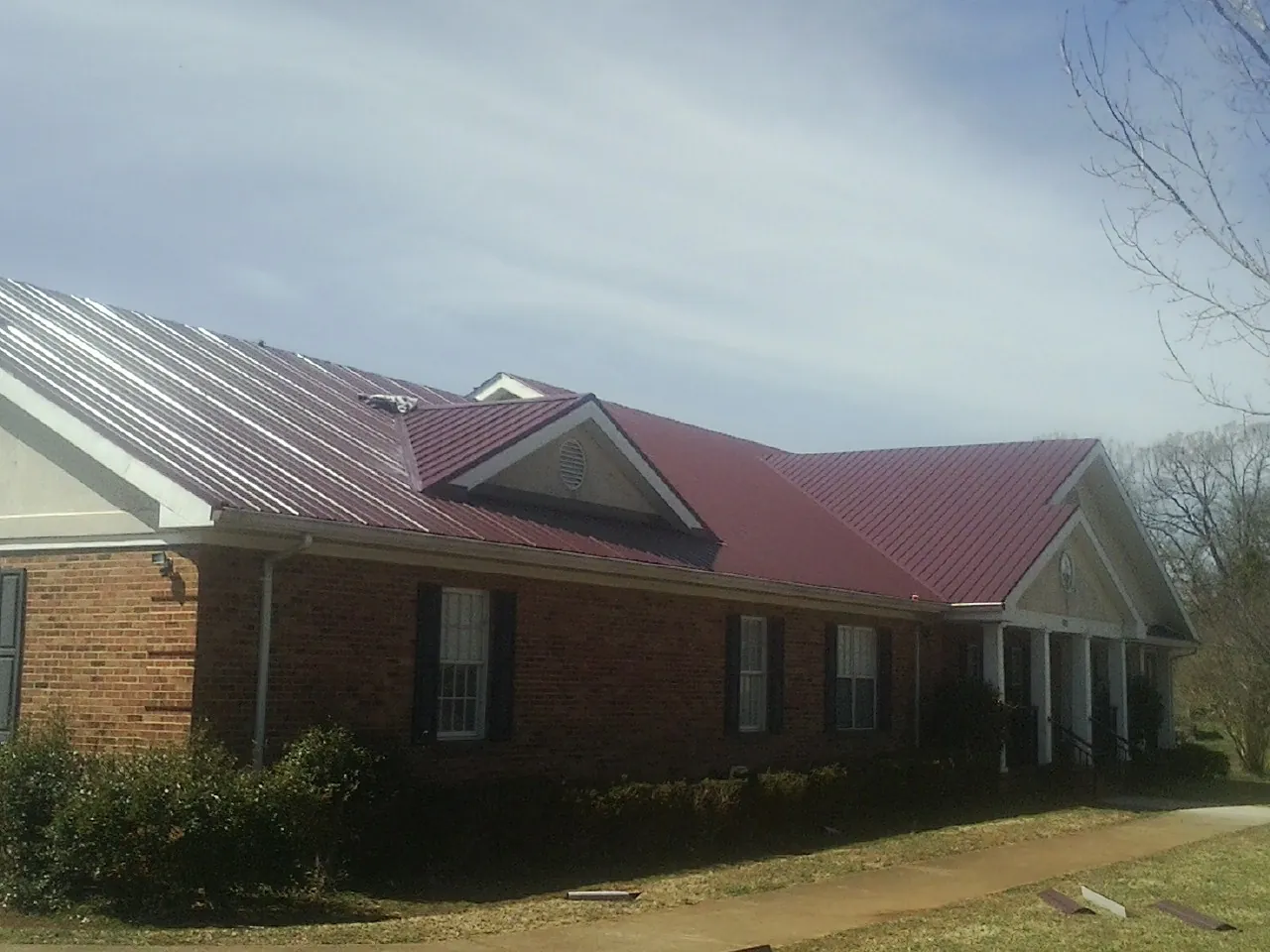 Red metal roof with gabled entries on a long brick building, from a Hail Damage Roof Repair job in Lynnwood