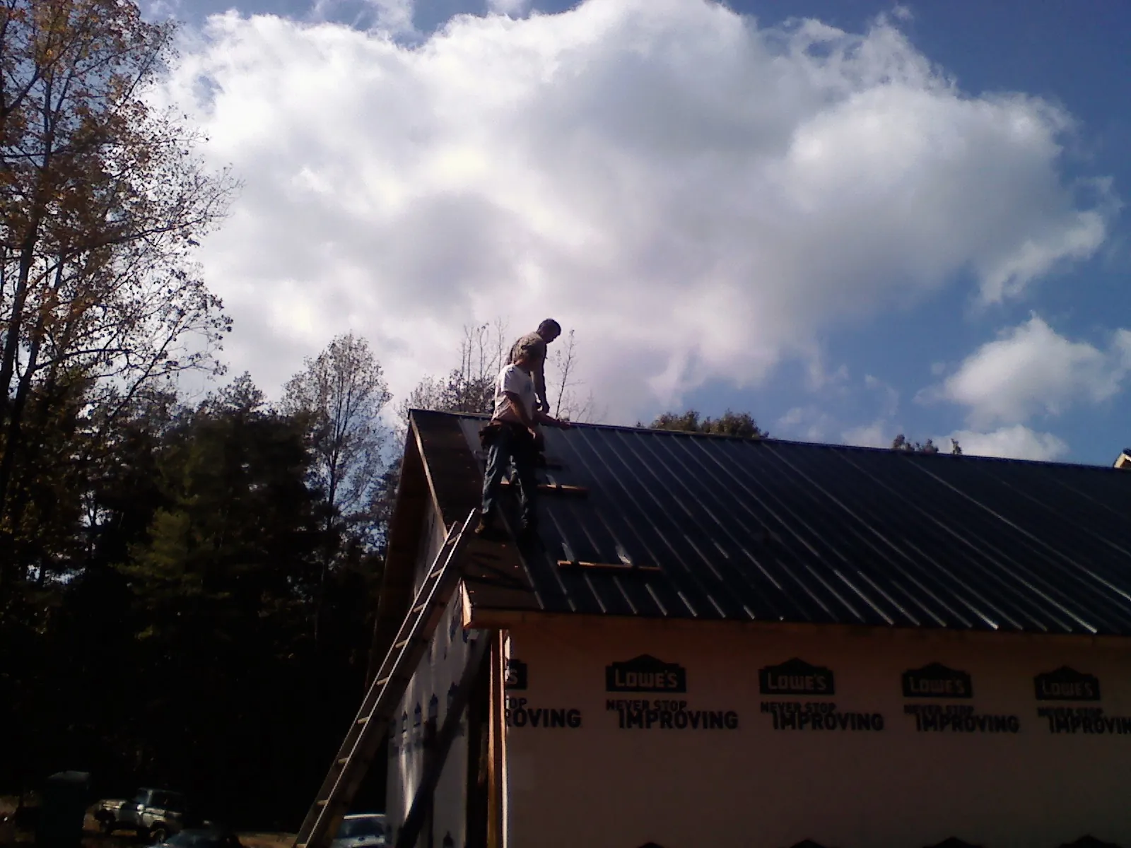 Roofer fastening dark metal panels high against a cloudy sky, from a Roof Inspection job in Lynnwood