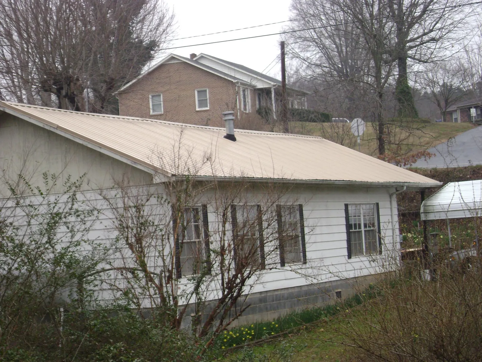 Tan metal roof on a white sided house set into a hillside — Commercial Roofing by Roofing Brothers in Lynnwood